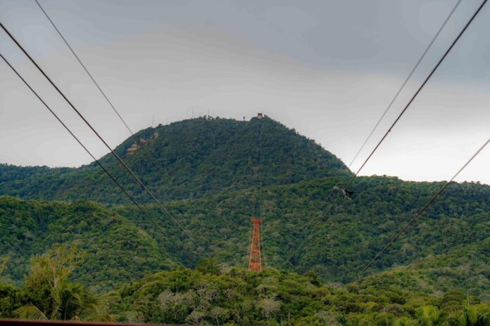 Gobierno inicia remozamiento integral del Teleférico de Puerto Plata La obra está a cargo de la empresa austriaca Doppelmayr Seilbahnen GmbH es la empresa líder a nivel mundial en la fabricación de teleféricos, funiculares y sistemas de transporte por cable. El proyecto renovará el sistema que opera desde 1975 con nuevas cabinas panorámicas para 55 pasajeros, mayor capacidad, accesibilidad y sistemas de seguridad de última generación, preservando su histórico recorrido hacia la Loma Isabel de Torres. Puerto Plata, República Dominicana, 3 de octubre de 2026.- El ministro de la Presidencia, José Ignacio Paliza, encabezó el inicio de los trabajos de modernización integral del Teleférico de Puerto Plata, una intervención que renovará este emblemático atractivo turístico luego de más de cinco décadas de servicio. La obra, a cargo de la Unidad para la Readecuación de Barrios y Entornos (URBE) conjuntamente con el Consorcio DOMA (integrado por la empresa austríaca Doppelmayr Seilbahnen GmbH y la constructora dominicana Grupo Malespín), contempla la sustitución del sistema actual por un moderno teleférico bicable de vaivén (ATW), con dos nuevas cabinas panorámicas para 55 pasajeros cada una, casi el triple de la capacidad actual, además de nuevos sistemas de accionamiento, control, monitoreo y seguridad. Durante el inicio de los trabajos, Paliza destacó que esta intervención forma parte de los esfuerzos del Gobierno para continuar fortaleciendo la infraestructura y las condiciones que acompañan el desarrollo turístico y económico de Puerto Plata. “La modernización del teleférico de Puerto Plata combina el valor histórico que tiene para esta provincia con una infraestructura más moderna, segura, accesible y con mayor capacidad para recibir a dominicanos y visitantes”, expresó Paliza. Explicó que la modernización contempla una renovación integral de los componentes esenciales del teleférico, manteniendo el recorrido que históricamente conecta con la Loma Isabel de Torres. “No se trata solamente de sustituir las cabinas. Estamos renovando el sistema de cable, los accionamientos, los controles y mecanismos de seguridad, la infraestructura eléctrica y las estaciones. El objetivo es entregar un teleférico con tecnología de nueva generación, mayor capacidad y mejores condiciones de accesibilidad y servicio para sus usuarios”, agregó el ministro. Doppelmayr Seilbahnen GmbH es la empresa líder a nivel mundial en la fabricación de teleféricos, funiculares y sistemas de transporte por cable. La compañía diseña, construye y da mantenimiento a medios de elevación para estaciones de esquí, zonas turísticas y sistemas de transporte público en ciudades. El director general del Instituto Dominicano de Aviación Civil (IDAC), Igor Rodríguez, destacó que la modernización permitirá contar con un sistema acorde con los más altos estándares de seguridad y confiabilidad. “Esta renovación representa un paso importante para garantizar que el Teleférico de Puerto Plata opere con tecnología de vanguardia y bajo rigurosos estándares de seguridad. Desde el IDAC, como miembros del Gabinete de Turismo, apoyamos este proceso, procurando que la nueva infraestructura reúna las condiciones técnicas necesarias para ofrecer a los usuarios un servicio seguro y confiable”, afirmó Rodríguez.